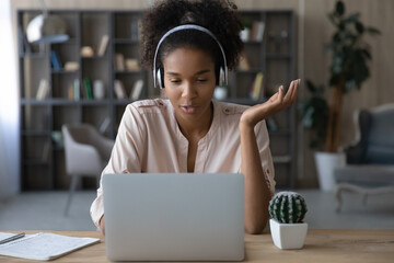 Close up African American woman in headphones chatting online, using laptop, sitting at work desk,...