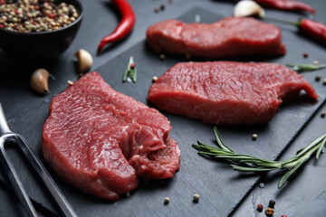 Fresh raw meat steaks and spices on black table, closeup