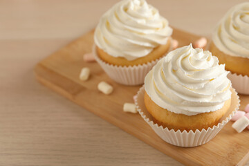 Delicious cupcakes with cream and marshmallows on wooden table, closeup. Space for text