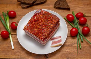 Smoked spicy bacon on a plate. Slice of smoked pork meat on bread, cherry tomatoes and green onion on wooden table.