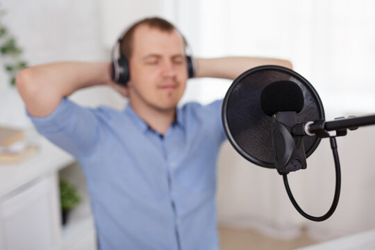 creativity, podcast and blogging concept - happy young man with microphone and headphones recording podcast at home