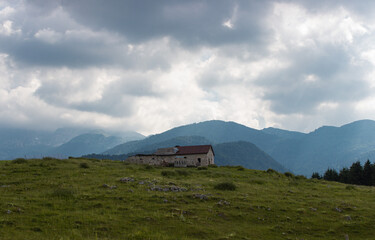 Mountain summer landscape. Small old stone barn with the background of the mountains. Cloudy and hazy day. Dramatic sky. Magical atmosphere. Valmenera, Belluno, Italy