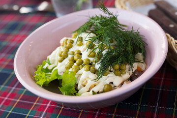 traditional Russian salad with peas and mayonnaise in a pink bowl