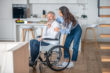 Young long-haired woman smiling nicely to her handicapped hausband and both looking happy