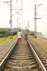 couple of young people hold hands and walk on railway tracks