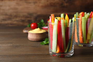 Fresh raw vegetable sticks in glasses on wooden table, space for text