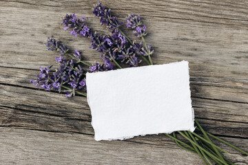 Summer floral stationery still life scene. Blank greeting card mock-up on old wooden table background with lavender flowers. Flat lay, top view. Mediterranean herbs, spa or wedding concept
