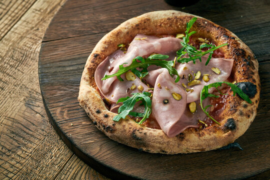 Pizza with mortadela, arugula and pistachios on a wooden board. Italian Cuisine
