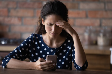 Worried Latin woman having problems with mobile phone, using wrong working apps, getting annoyed...