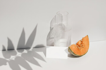Summer food still life composition. Cantaloupe melon fruit on table. White wall with palm leaf...
