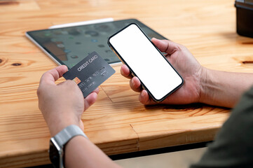 Man's hands holding a credit card and using smart phone for online shopping