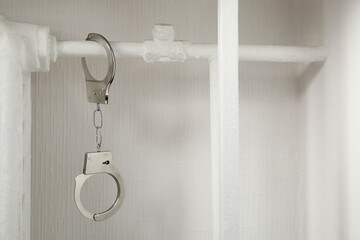 Handcuffs hanging on radiator near white wall indoors
