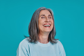 Headshot of mature beautiful woman laughing while standing against blue background