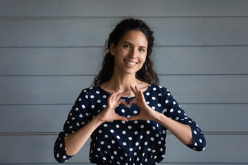 Happy grateful millennial Hispanic woman showing love hand gesture, making finger heart, symbol of romance, gratitude, charity, support, kindness. Donation campaign, awareness day concept