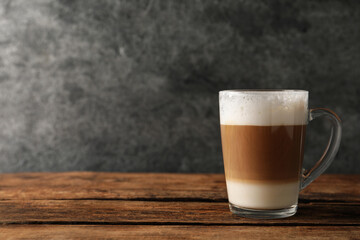 Glass cup of delicious layered coffee on wooden table against grey background, space for text