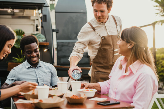 Happy People Having Fun Eating At Food Truck Restaurant Outdoor In The City - Focus On Waiter Face