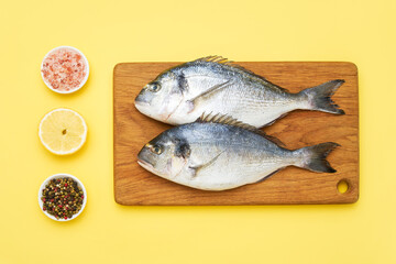 Raw dorado fish with spices on a wooden cutting board on a yellow background