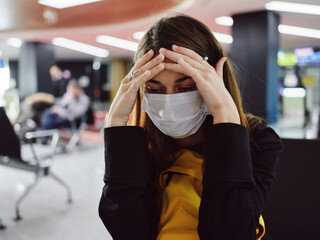 woman holding her head in a medical mask tiredness waiting for a flight airport