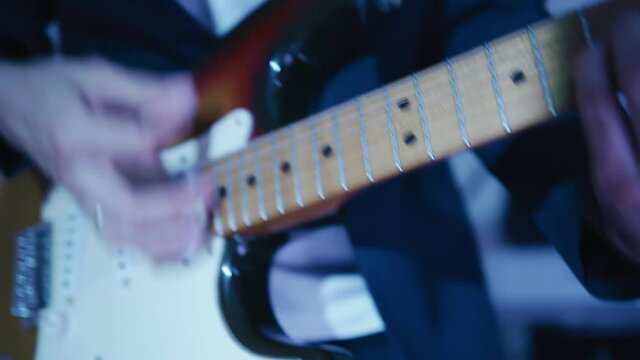 The guitarist dynamically plays the guitar at a performance on stage. Shooting of tools and hands in close-up ple