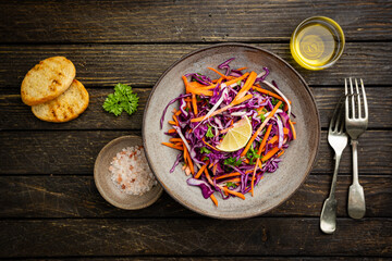 Fresh coleslaw salad made of shredded red and white cabbage and carrots on dark wooden background, top view