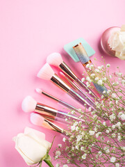 Obraz na płótnie Canvas Trendy make up brushes with products on pink background with gypsophila flowers