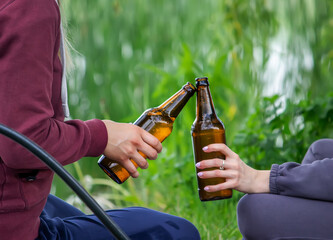 The hand of a man holding a beer bottle in nature. rest by the river. Selective focus