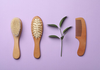 Wooden brushes and plant on violet background, flat lay. Conscious consumption