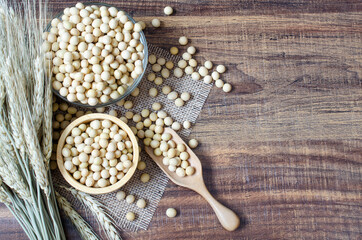 Group of dry organic soybean seed in wooden bowl and spoon on sack fabric and wooden background with dry wheat ear