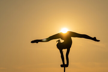 Silhouette of flexible acrobat doing handstand on the dramatic sunset background. Concept of individuality, creativity and passion