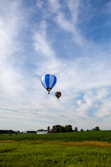 Obraz premium Near Wausau, Wisconsin, USA, July 10, 2021, Taste N Glow Balloon Fest. Two hot air balloons in the the sky looking for a place to land in a famers field
