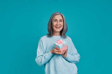 Mature beautiful woman looking at camera and smiling while standing against blue background