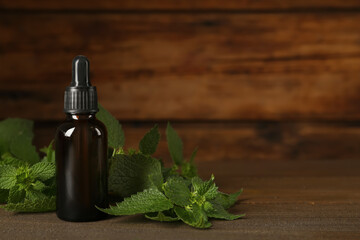 Glass bottle of nettle oil with dropper and leaves on wooden table, space for text