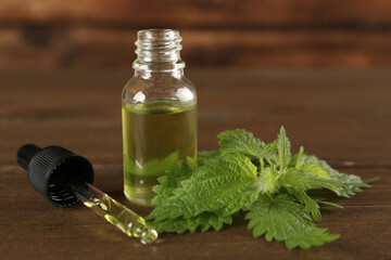 Fresh nettle leaves near glass bottle and pipette with oil on wooden table, closeup