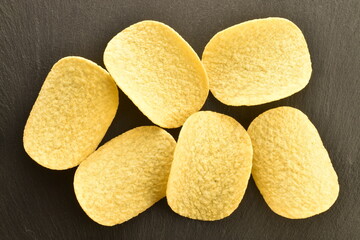 Several potato chips on a serving slate board, close-up, top view.