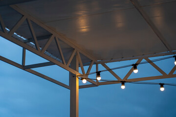 Textile visor on canopy with garland of energy saving lamps illuminating terrace of restaurant of night city