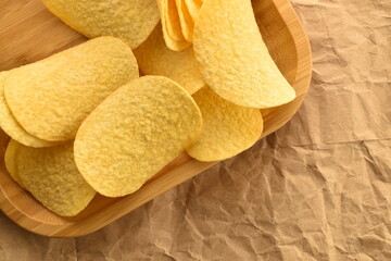 Several potato chips in a bamboo plate on craft paper, close-up, top view.
