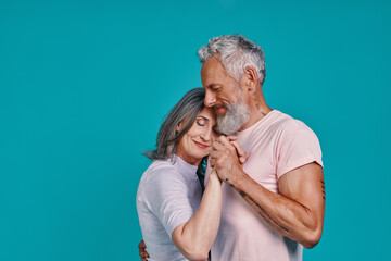 Romantic senior couple dancing and smiling while standing together against blue background