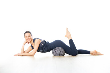 Fototapeta na wymiar Restorative yoga with a bolster. Young sporty female yoga instructor in bright white yoga studio, lying on bolster cushion, stretching, smilling, showing love and passion for restorative yoga