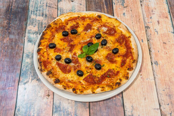 Thin crust pizza with black olives, basil, chunks of spicy chorizo and mozzarella cheese on white plate and wooden table.