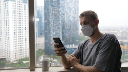 Bored and lonely white man in a face mask going through his phone while quarantining