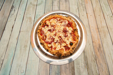 Well-cooked diavola pizza with red onion, spicy salami, melted mozzarella cheese and tomato on metal tray