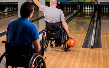 Two young disabled men in wheelchairs playing bowling in the club