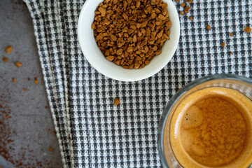 Glass cup of espresso coffee with ground coffee beans placed on a plaid towel. Top view