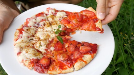 A hand picking a slice of vegan pizza topped with dairy free cheese and strawberries. Plant based hipster street food