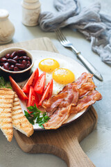 Traditional full English breakfast with fried eggs, sausages, beans, grilled tomatoes and bacon on gray concrete background. Top view