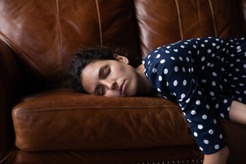 Tired peaceful millennial Latin woman with closed eyes lying on soft cozy sofa, sleeping at...