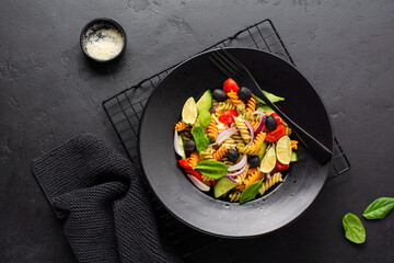 Whole grain pasta with vegetables on a white plate on black slate, stone or concrete background. Top view with copy space.