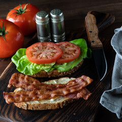 Close up of an open bacon and tomato sandwich against a dark background.
