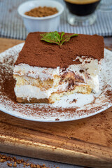 Slice of eaten traditional tiramisu cake with a cup of coffee in the background. Authentic gluten-free Italian layered dessert with ladyfinger biscuits, mascarpone cheese cream and cocoa powder. Side