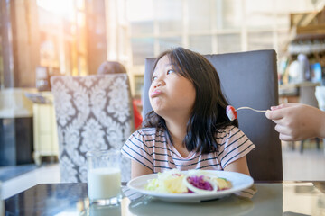 asian child girl with expression of disgust against tomato in salad,